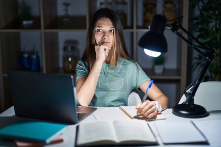 Téléchargez les photos : Teenager girl doing homework at home late at night thinking worried about a question, concerned and nervous with hand on chin - en image libre de droit