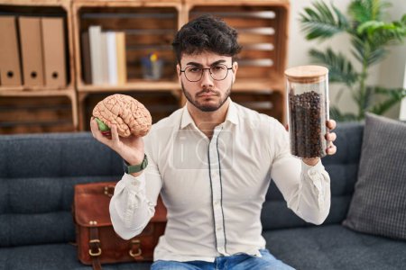 Photo for Hispanic man with beard working at therapy office holding brain and coffee beans skeptic and nervous, frowning upset because of problem. negative person. - Royalty Free Image