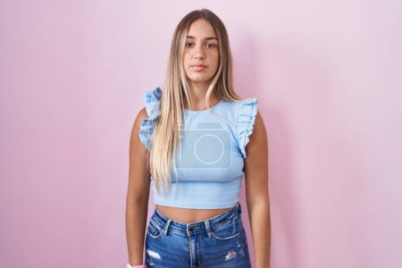 Photo for Young blonde woman standing over pink background relaxed with serious expression on face. simple and natural looking at the camera. - Royalty Free Image