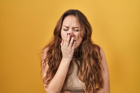 Photo for Young hispanic woman standing over yellow background bored yawning tired covering mouth with hand. restless and sleepiness. - Royalty Free Image