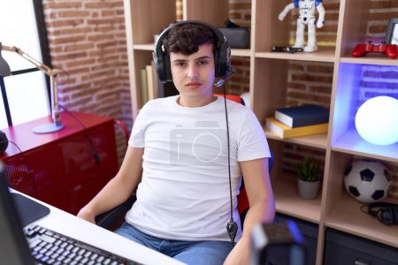 Photo for Non binary man streamer sitting on table with relaxed expression at gaming room - Royalty Free Image