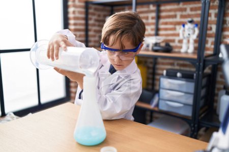 Foto de Adorable hispanic boy student pouring liquid on test tube at laboratory classroom - Imagen libre de derechos