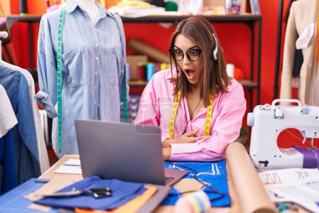 Photo for Young hispanic woman dressmaker designer doing video call with laptop scared and amazed with open mouth for surprise, disbelief face - Royalty Free Image