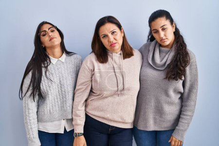 Photo for Mother and two daughters standing over blue background looking sleepy and tired, exhausted for fatigue and hangover, lazy eyes in the morning. - Royalty Free Image