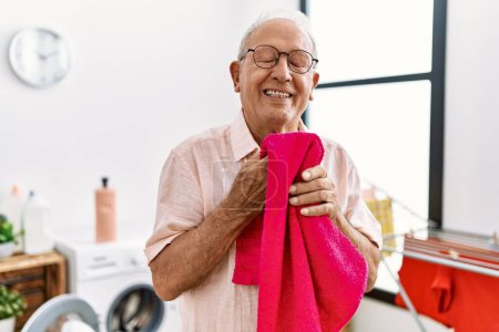 Téléchargez les photos : Senior homme souriant confiant serviette odorante à la buanderie - en image libre de droit