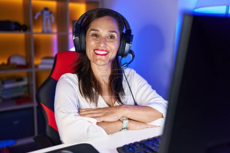 Foto de Mujer morena de mediana edad jugando videojuegos cara feliz sonriendo con los brazos cruzados mirando a la cámara. persona positiva. - Imagen libre de derechos