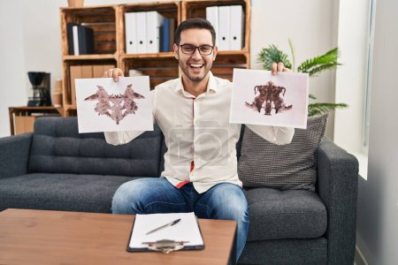 Foto de Young hispanic man with beard holding rorschach test smiling and laughing hard out loud because funny crazy joke. - Imagen libre de derechos