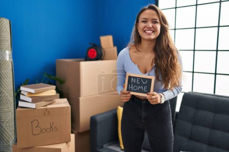 Photo for Young hispanic woman holding blackboard with new home text looking positive and happy standing and smiling with a confident smile showing teeth - Royalty Free Image