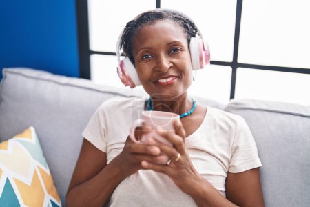 Téléchargez les photos : Moyen Age femme afro-américaine écouter de la musique boire du café à la maison - en image libre de droit