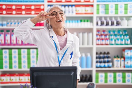 Téléchargez les photos : Middle age woman with tattoos working at pharmacy drugstore doing peace symbol with fingers over face, smiling cheerful showing victory - en image libre de droit
