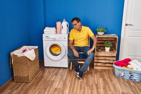Photo for Middle age man sitting on chair waiting for washing machine at laundry room - Royalty Free Image