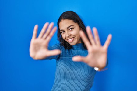 Téléchargez les photos : Jeune femme brésilienne debout sur fond bleu isolé faisant cadre en utilisant les mains paumes et les doigts, perspective de la caméra - en image libre de droit