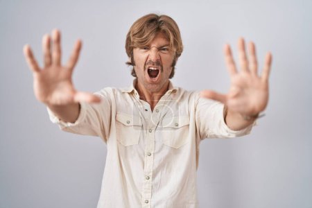Foto de Middle age man standing over isolated background doing stop gesture with hands palms, angry and frustration expression - Imagen libre de derechos