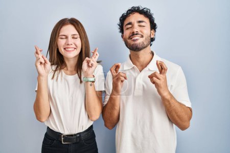 Foto de Young couple wearing casual clothes standing together gesturing finger crossed smiling with hope and eyes closed. luck and superstitious concept. - Imagen libre de derechos