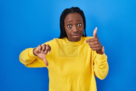 Photo for Beautiful black woman standing over blue background doing thumbs up and down, disagreement and agreement expression. crazy conflict - Royalty Free Image