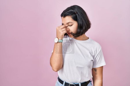 Foto de Mujer hispana joven con camiseta blanca casual sobre fondo rosa cansada frotando nariz y ojos sintiendo fatiga y dolor de cabeza. concepto de estrés y frustración. - Imagen libre de derechos