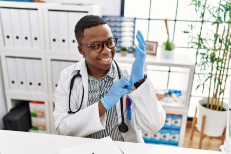 Téléchargez les photos : Jeune homme africain travaillant comme médecin utilisant des gants à la clinique médicale - en image libre de droit