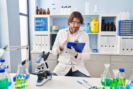 Téléchargez les photos : Middle age man scientist holding test tube reading document at laboratory - en image libre de droit
