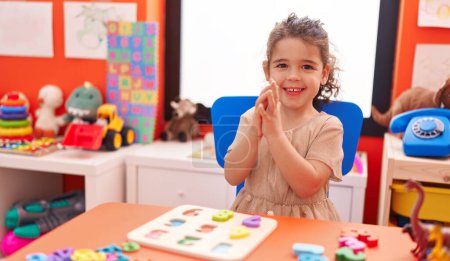 Foto de Adorable hispanic girl playing with maths puzzle game clapping hands at kindergarten - Imagen libre de derechos