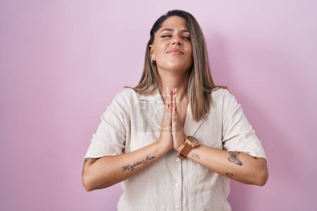 Photo for Blonde woman standing over pink background begging and praying with hands together with hope expression on face very emotional and worried. begging. - Royalty Free Image