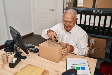 Téléchargez les photos : Senior man ecommerce business worker opening package at office - en image libre de droit