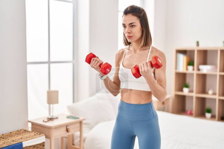 Photo for Young beautiful hispanic woman using dumbbells training at bedroom - Royalty Free Image