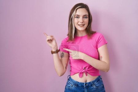 Téléchargez les photos : Blonde caucasian woman standing over pink background smiling and looking at the camera pointing with two hands and fingers to the side. - en image libre de droit