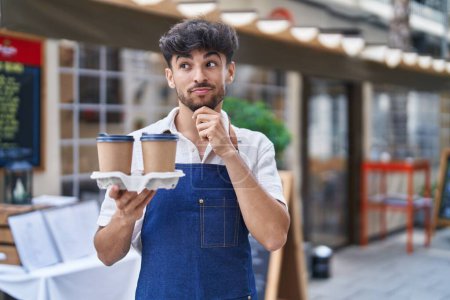Photo for Arab man with beard wearing waiter apron at restaurant terrace serious face thinking about question with hand on chin, thoughtful about confusing idea - Royalty Free Image
