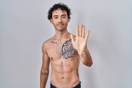 Téléchargez les photos : Hispanic man standing shirtless showing and pointing up with fingers number five while smiling confident and happy. - en image libre de droit