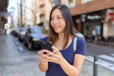 Téléchargez les photos : Jeune femme asiatique souriant confiant en utilisant smartphone à la rue - en image libre de droit