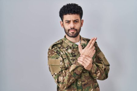 Photo for Arab man wearing camouflage army uniform holding symbolic gun with hand gesture, playing killing shooting weapons, angry face - Royalty Free Image