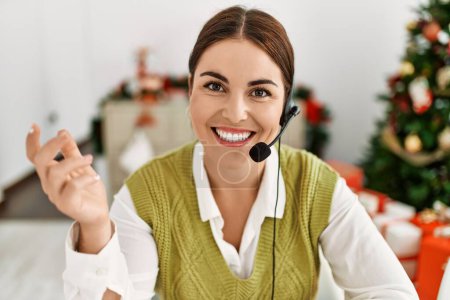 Photo for Young beautiful hispanic woman call center agent sitting by christmas tree speaking at home - Royalty Free Image