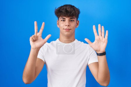 Foto de Hispanic teenager standing over blue background showing and pointing up with fingers number eight while smiling confident and happy. - Imagen libre de derechos