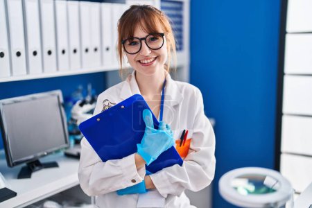 Foto de Young woman scientist smiling confident holding clipboard at laboratory - Imagen libre de derechos