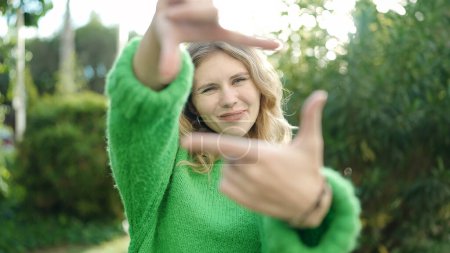 Foto de Young blonde woman smiling confident doing photo gesture with hands at park - Imagen libre de derechos
