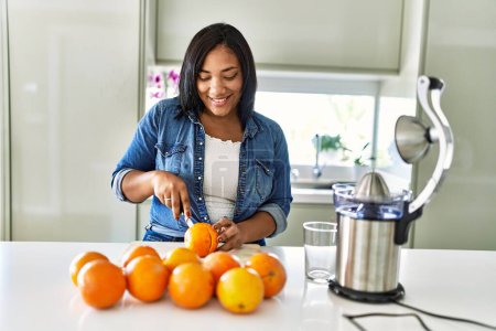 Foto de Hispanic brunette woman cutting oranges for juice at the kitchen - Imagen libre de derechos