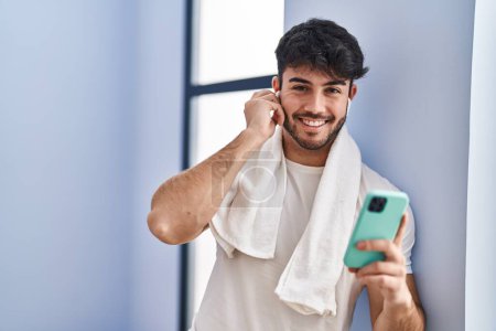 Téléchargez les photos : Jeune homme hispanique souriant confiant écoutant de la musique au centre sportif - en image libre de droit