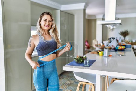 Photo for Young woman smiling confident measuring waist using tape measure at kitchen - Royalty Free Image