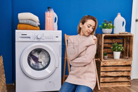 Téléchargez les photos : Young woman hugging himself waiting for washing machine at laundry room - en image libre de droit