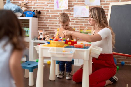 Foto de Teacher and toddler playing with construction blocks sitting on table at kindergarten - Imagen libre de derechos