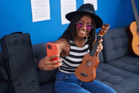 Foto de Afro americana mujer músico holding ukelele fabricación selfie por smartphone en música studio - Imagen libre de derechos