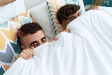 Foto de Dos hombres hispanos pareja acostada en la cama cubriendo la cara con manta en el dormitorio - Imagen libre de derechos