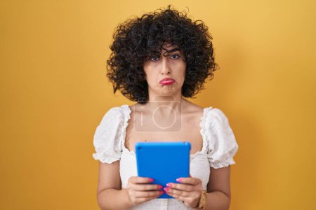 Foto de Young brunette woman with curly hair using touchpad over yellow background depressed and worry for distress, crying angry and afraid. sad expression. - Imagen libre de derechos