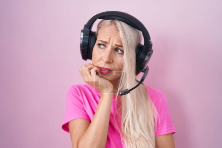 Photo for Caucasian woman listening to music using headphones looking stressed and nervous with hands on mouth biting nails. anxiety problem. - Royalty Free Image