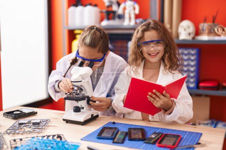 Foto de Dos estudiantes de niños usando escritura de microscopio en un cuaderno en el aula de laboratorio - Imagen libre de derechos