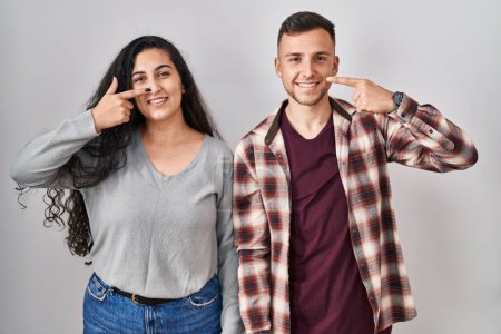 Téléchargez les photos : Young hispanic couple standing over white background pointing with hand finger to face and nose, smiling cheerful. beauty concept - en image libre de droit