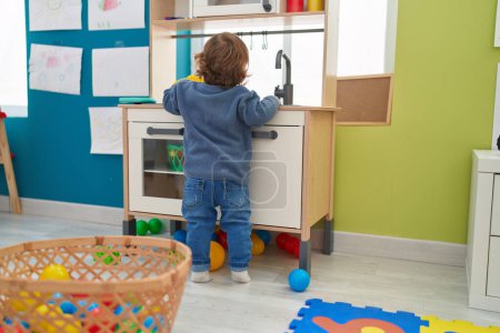 Foto de Adorable hispanic toddler playing with play kitchen standing at kindergarten - Imagen libre de derechos