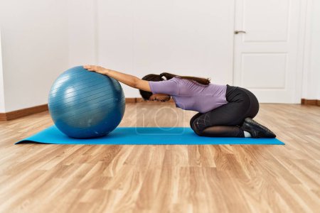 Photo for Young latin woman stretching using fit ball at sport center - Royalty Free Image