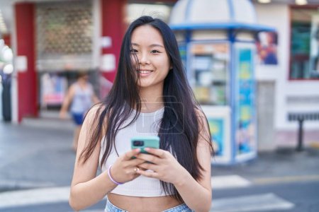 Foto de Young chinese woman smiling confident using smartphone at street - Imagen libre de derechos