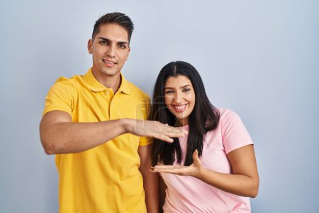 Photo for Young couple standing over isolated background gesturing with hands showing big and large size sign, measure symbol. smiling looking at the camera. measuring concept. - Royalty Free Image